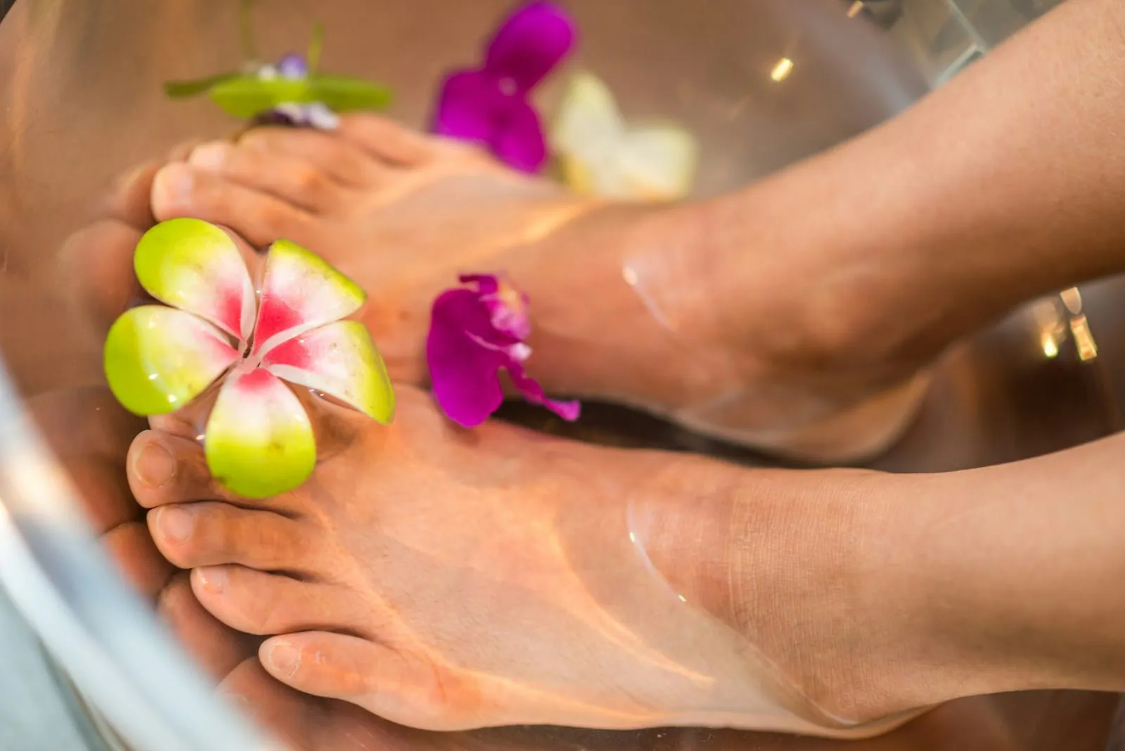 Feet resting in a warm foot bath decorated with pink and purple flowers